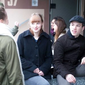 Ein junges Mädchen und ein junger Mann mit einer Mütze sitzen mit Freunden auf einer Bank