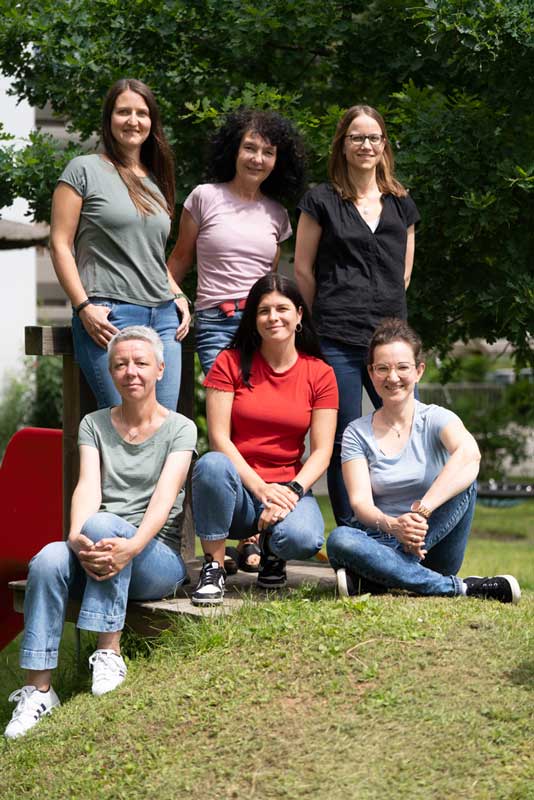 Sechs junge Fragen sitzen im Garten und lächeln in die Kamera.