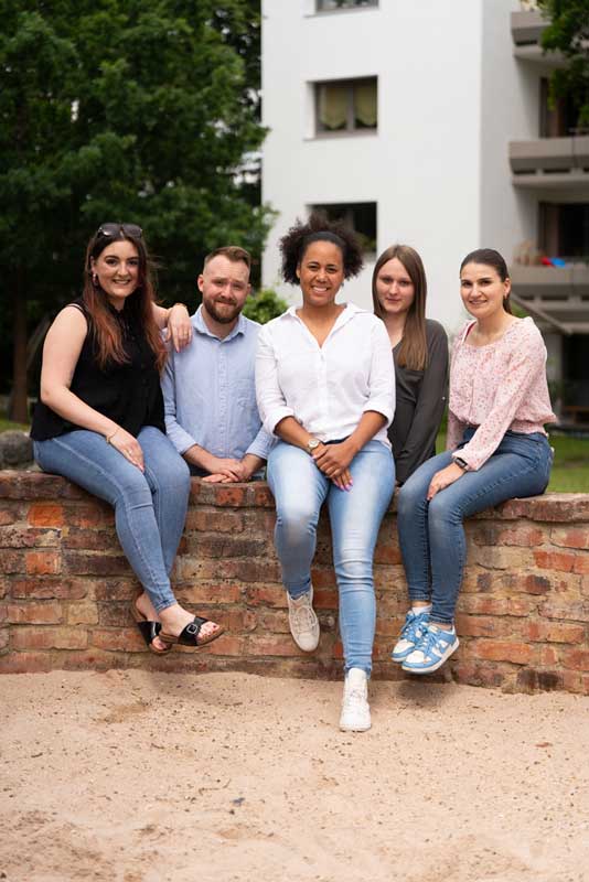 Vier Frauen und ein junger Mann sitzen auf einem Gartenmäuerchen und lächeln in die Kamera.