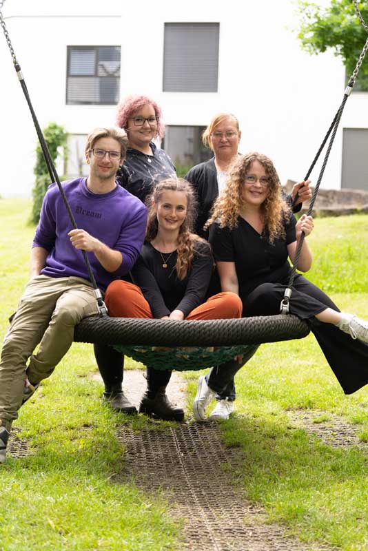 Vier Frauen und ein junger Mann sitzen auf einer Gartenschaukel lächeln in die Kamera.