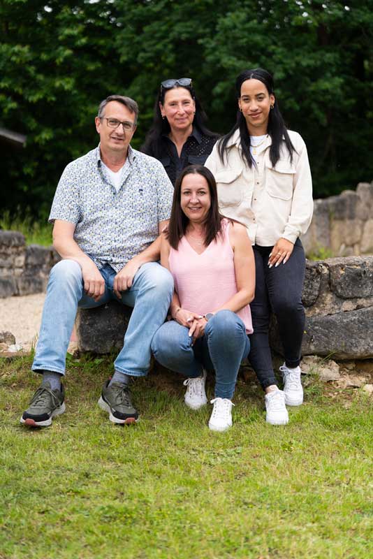 Drei Frauen und ein Mann sitzen im Garten und lächeln in die Kamera.