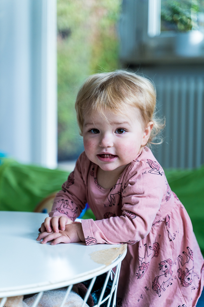 Ein kleines Mädchen mit einem rosa Kleid schaut in die Kamera