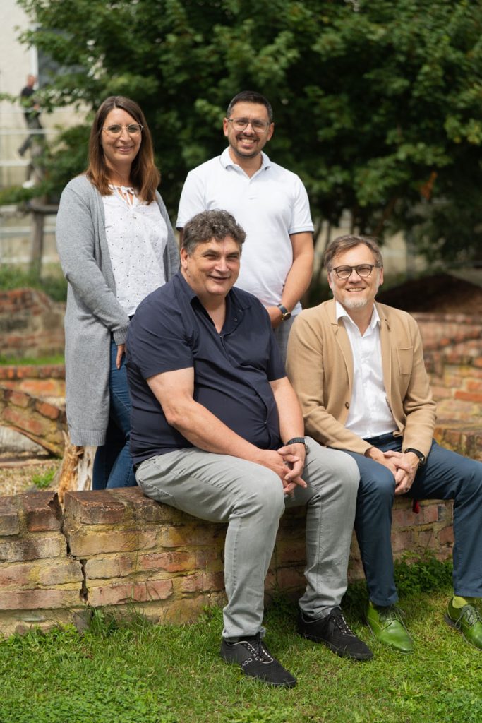 Drei Männer und eine Frau im Garten, sie lächeln in die Kamera