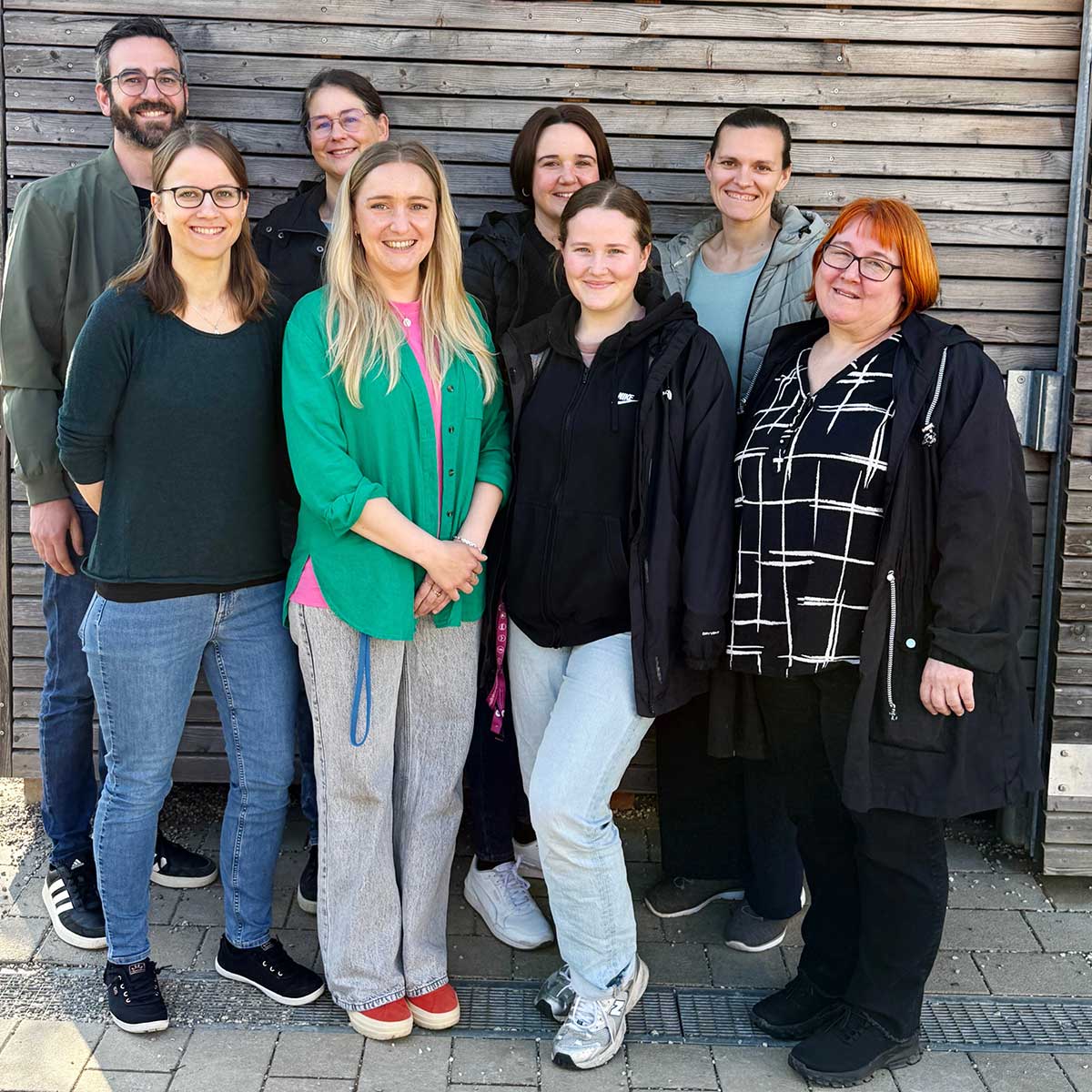 Eine Gruppe von Menschen vor einer Holzwand - das Team unserer Stütz- und Förderklassen