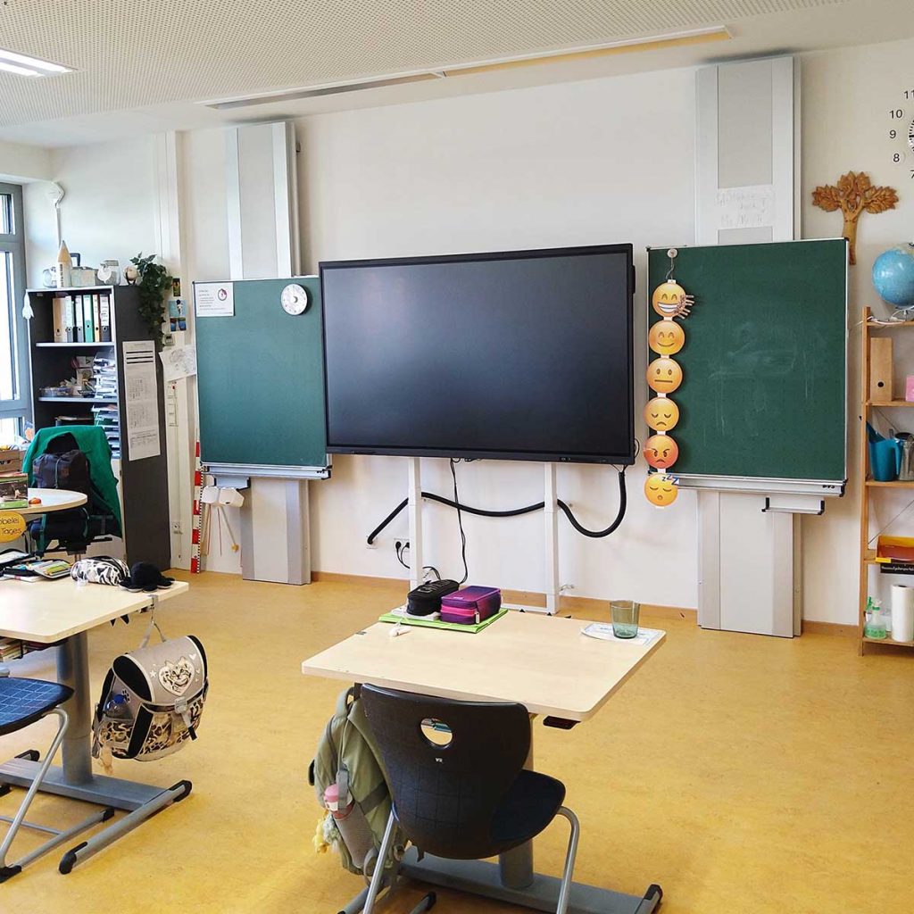Die Frontseite eines Klassenraums, mit einen großen Bildschirm und Tafeln.