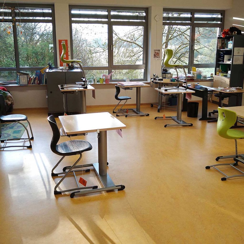 Ein heller Klassenraum mit kleinen Tischen und jeweils einem Stuhl