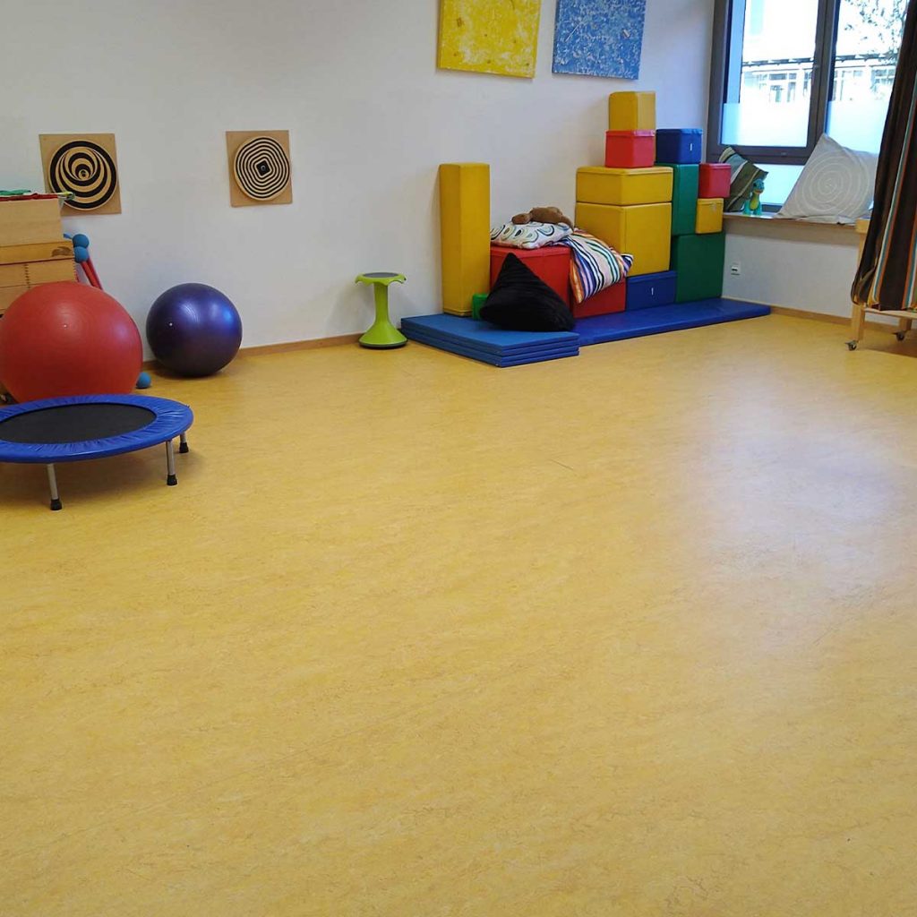 Ein Sportraum mit gelbem Boden, im Hintergrund Matten